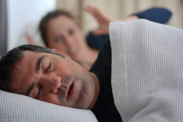 woman annoyed because her husband is snoring while asleep in bed