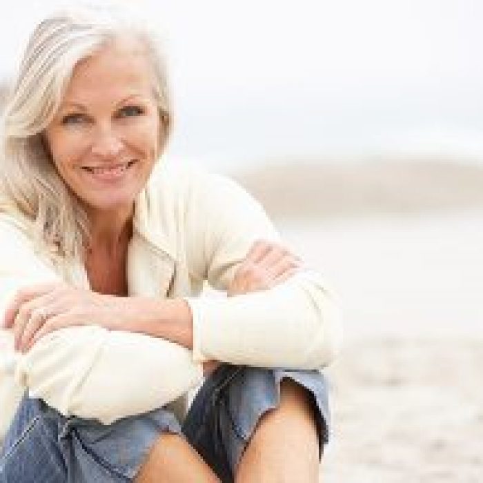older woman sitting on beach smiling